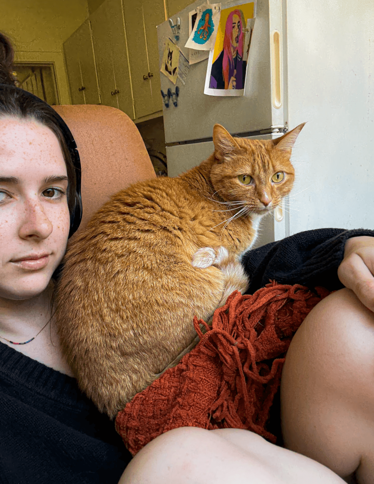Kathryn sitting at her desk with a red blanket and her orange cat, Topi, sitting on her knees