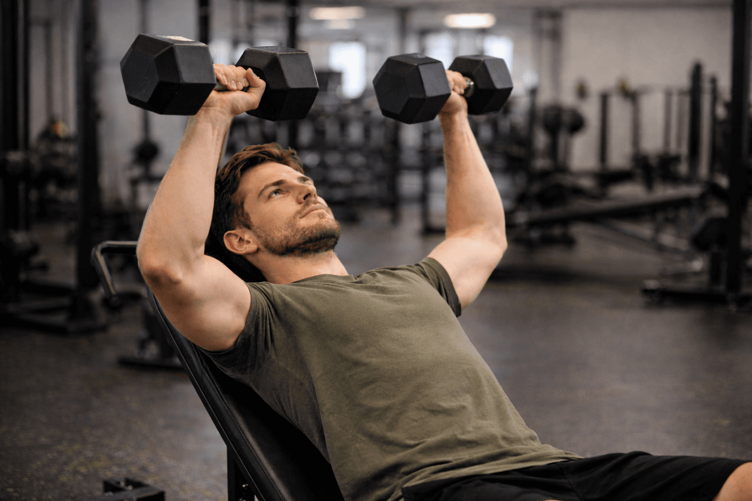 Man performing an incline dumbbell chest press in a gym to build upper body strength.