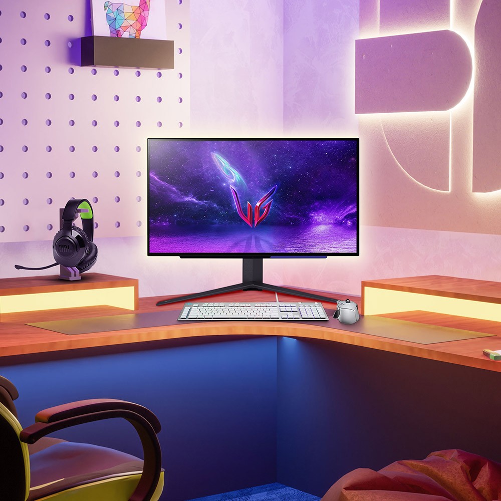 A gamer's room is illuminated by colorful lights. A computer chair, desk, speakers, monitors and few other electronics.