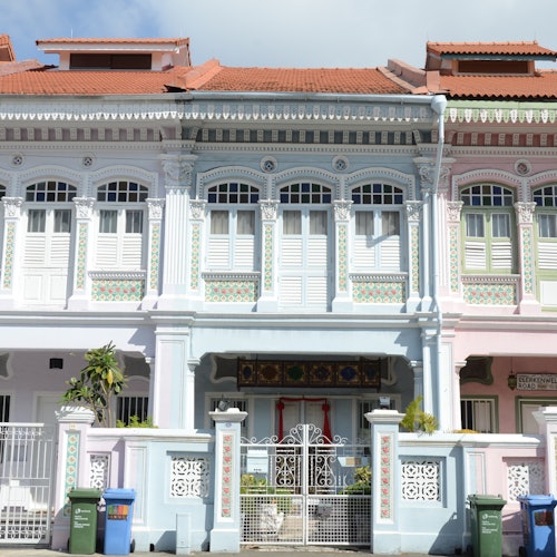 A row of pastel-colored townhouses with detailed architectural designs, including white shutters, ornate trim, and small balconies.