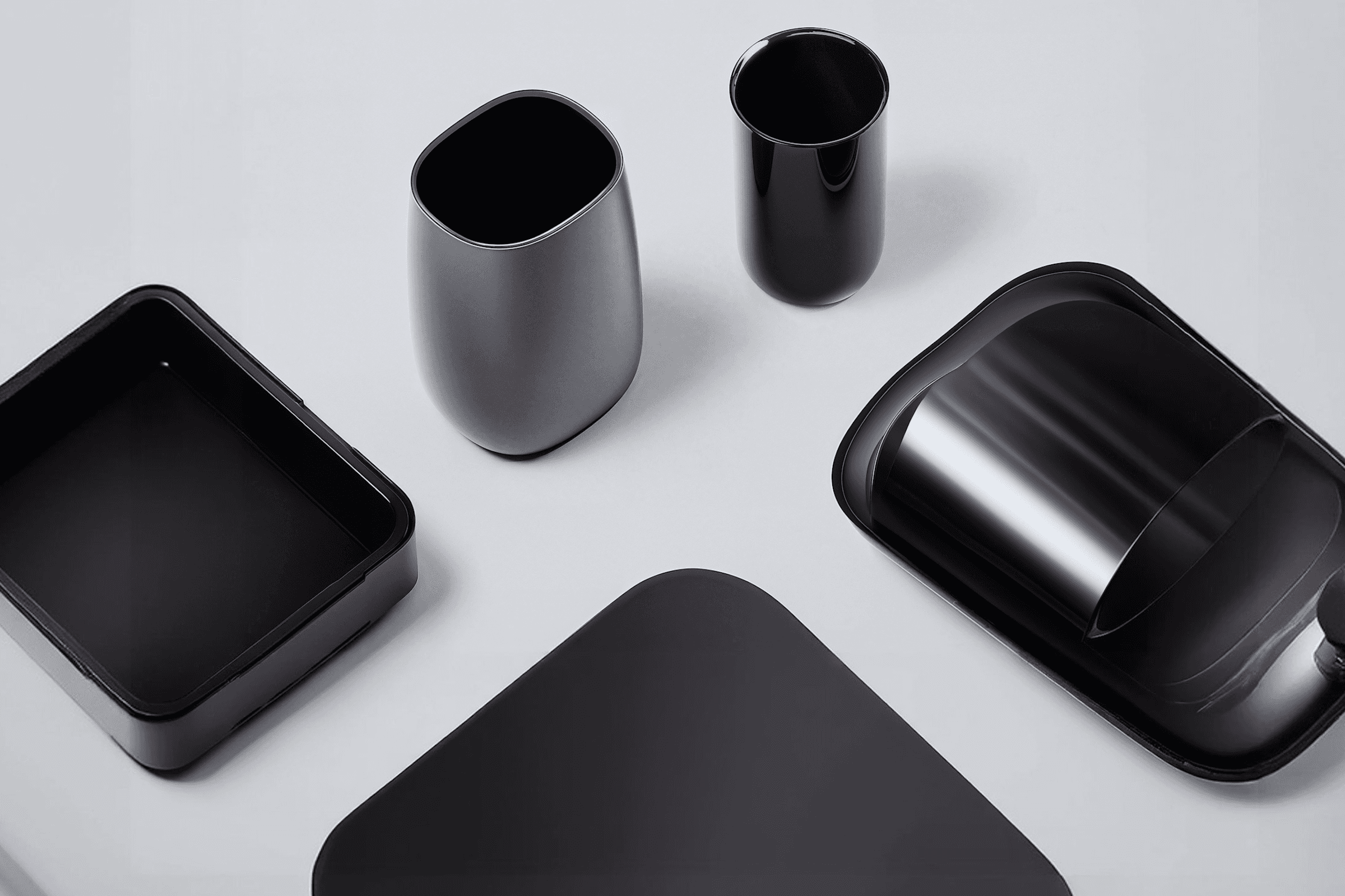 Sleek modern containers and trays in black and gray on a light gray surface, showcasing minimalist design and elegance.