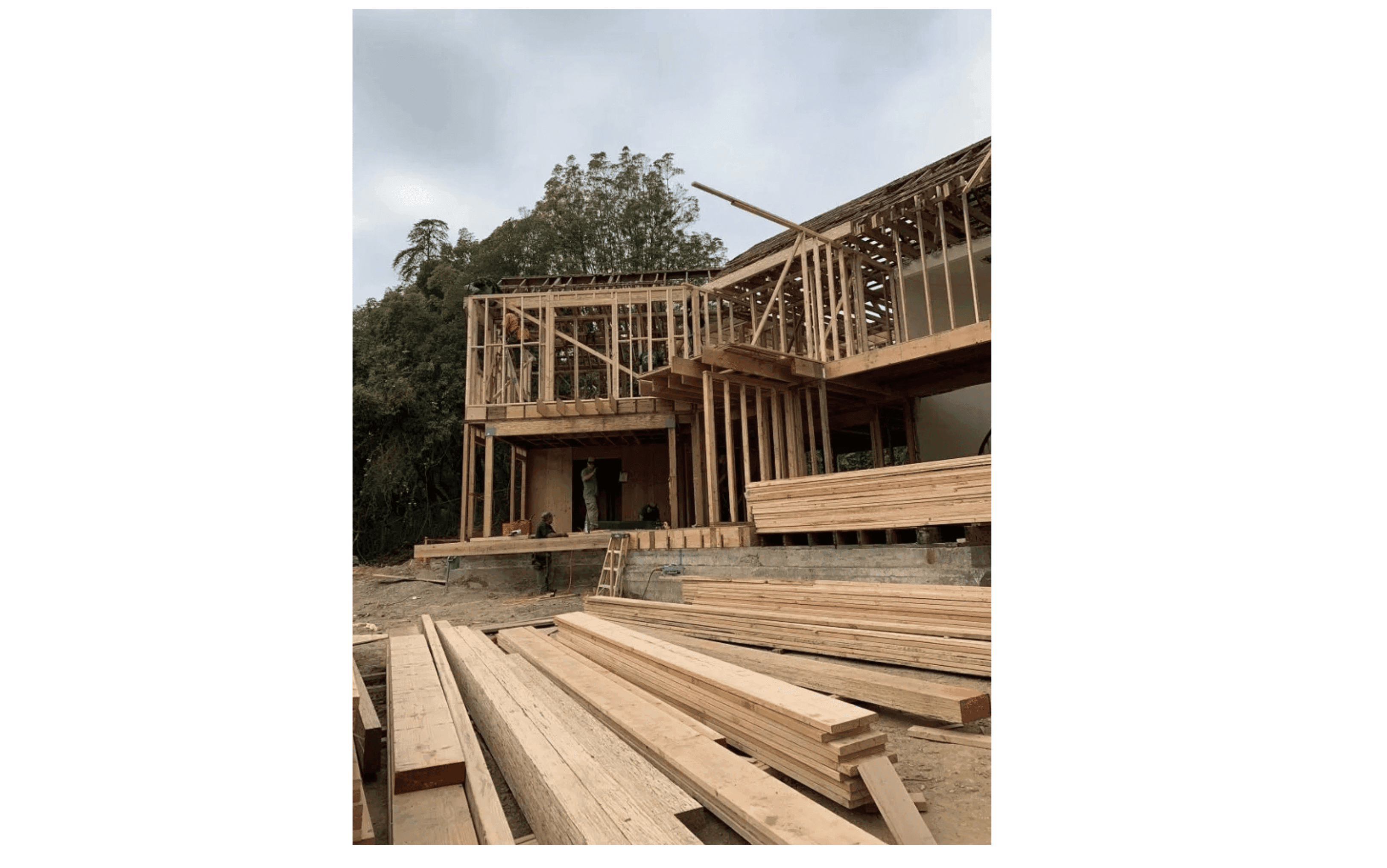 Wooden framing of a multi-story house under construction with stacks of lumber in the foreground