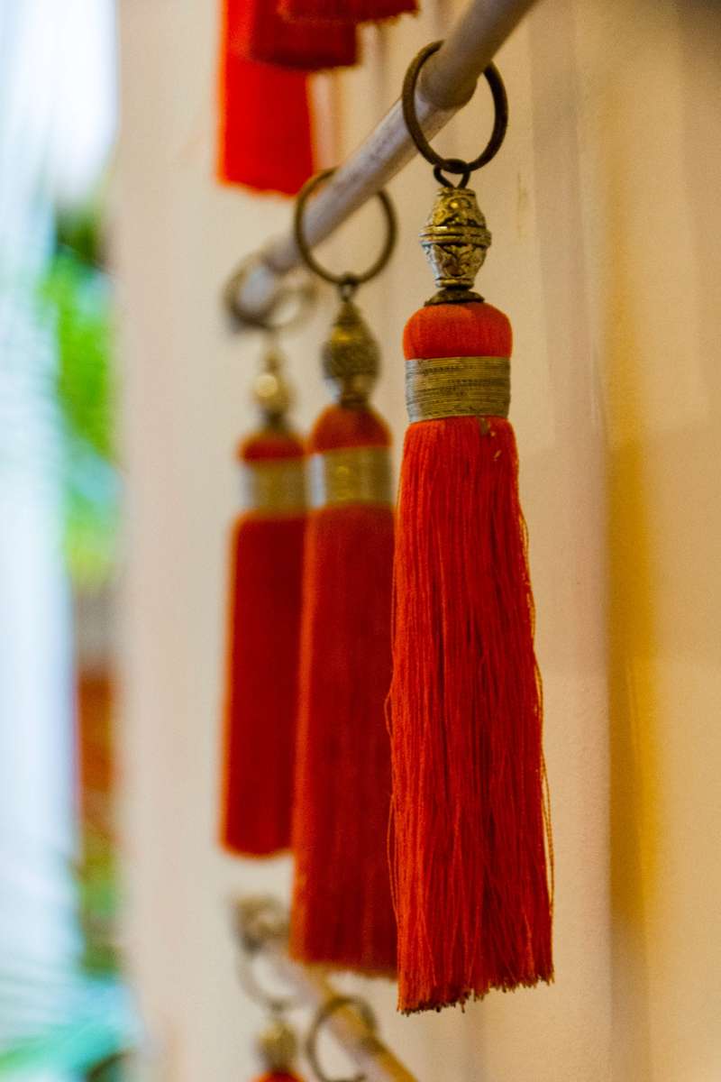 Red and gold tassels hang from a horizontal metal rod against a blurred background of yellow and green tones.