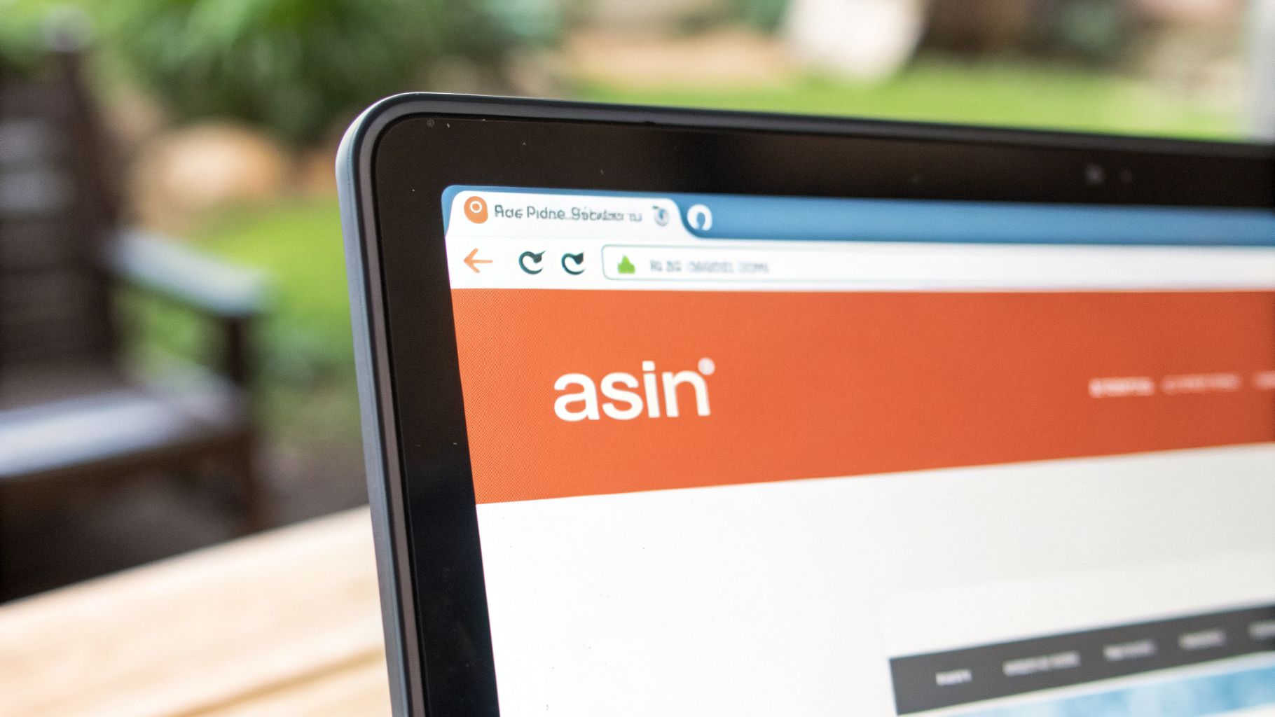 Close-up of a laptop screen displaying a website with the 'asin' logo on an orange header, outdoors.