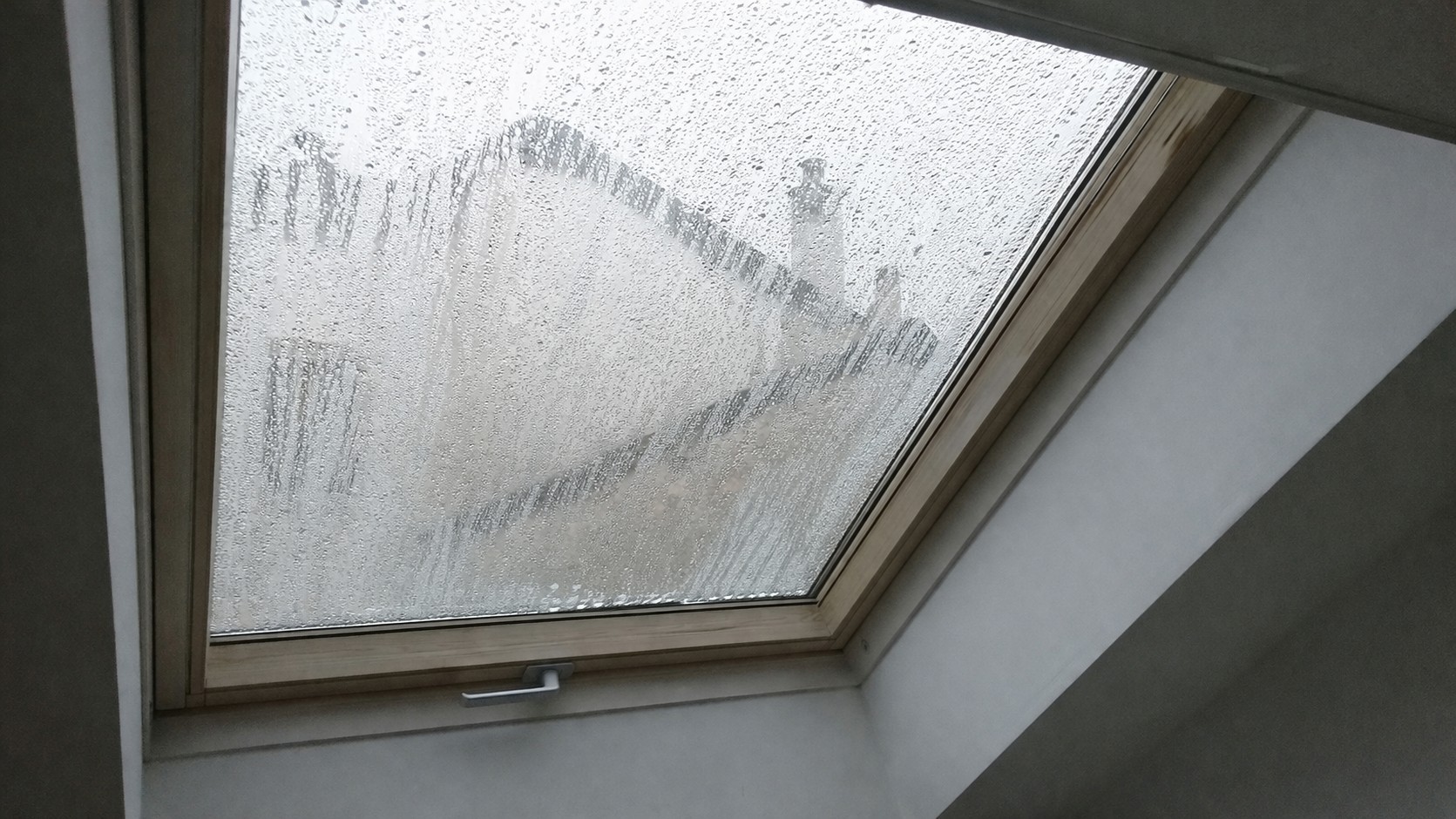 Photo d’un Velux avec condensation excessive sur la vitre, traces d’humidité visibles à l’intérieur sous toiture inclinée dans une maison