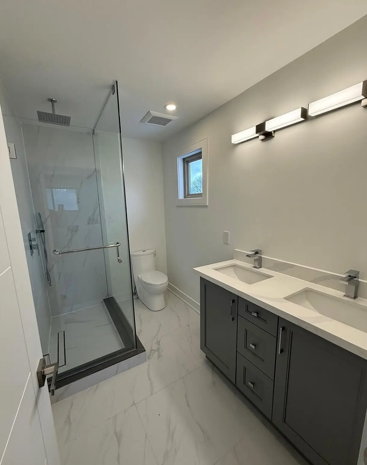 A professionally cleaned bathroom showcasing a dust-free exhaust vent, sanitized grey vanity, and polished marble floors following a post-construction deep clean.