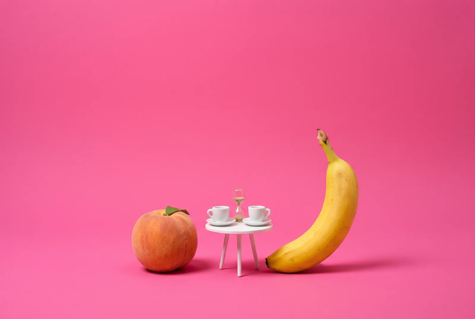 Weekly accountability partner check-in concept: a peach and a banana facing each other across a tiny café table with two espresso cups on a hot pink backdrop