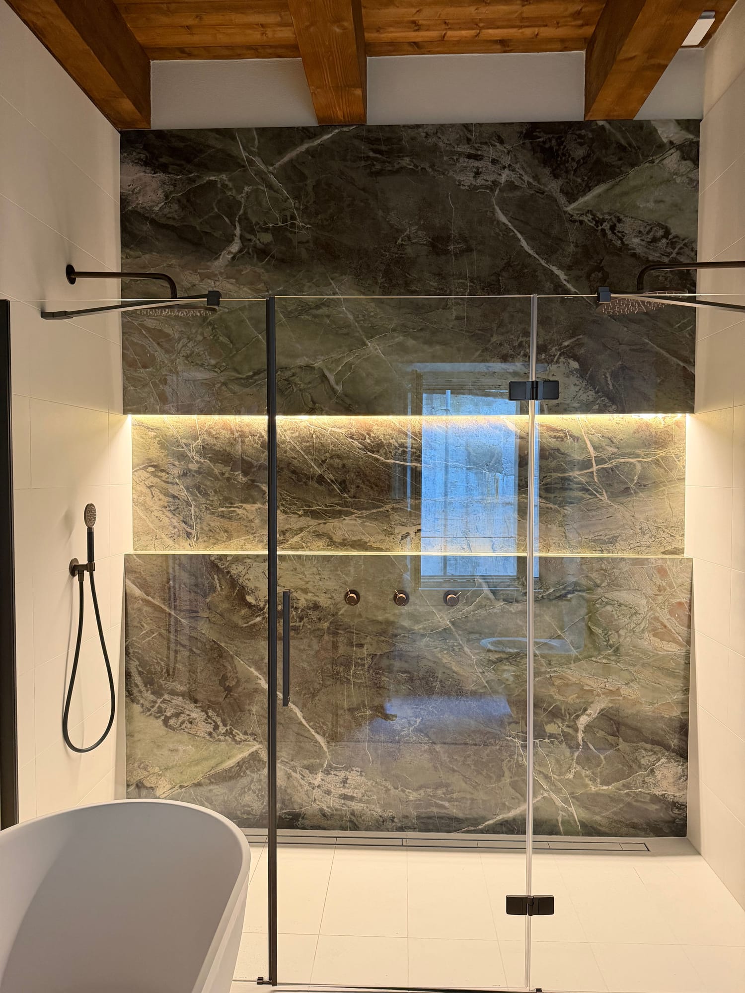 Shower clad in green marble with a freestanding bath