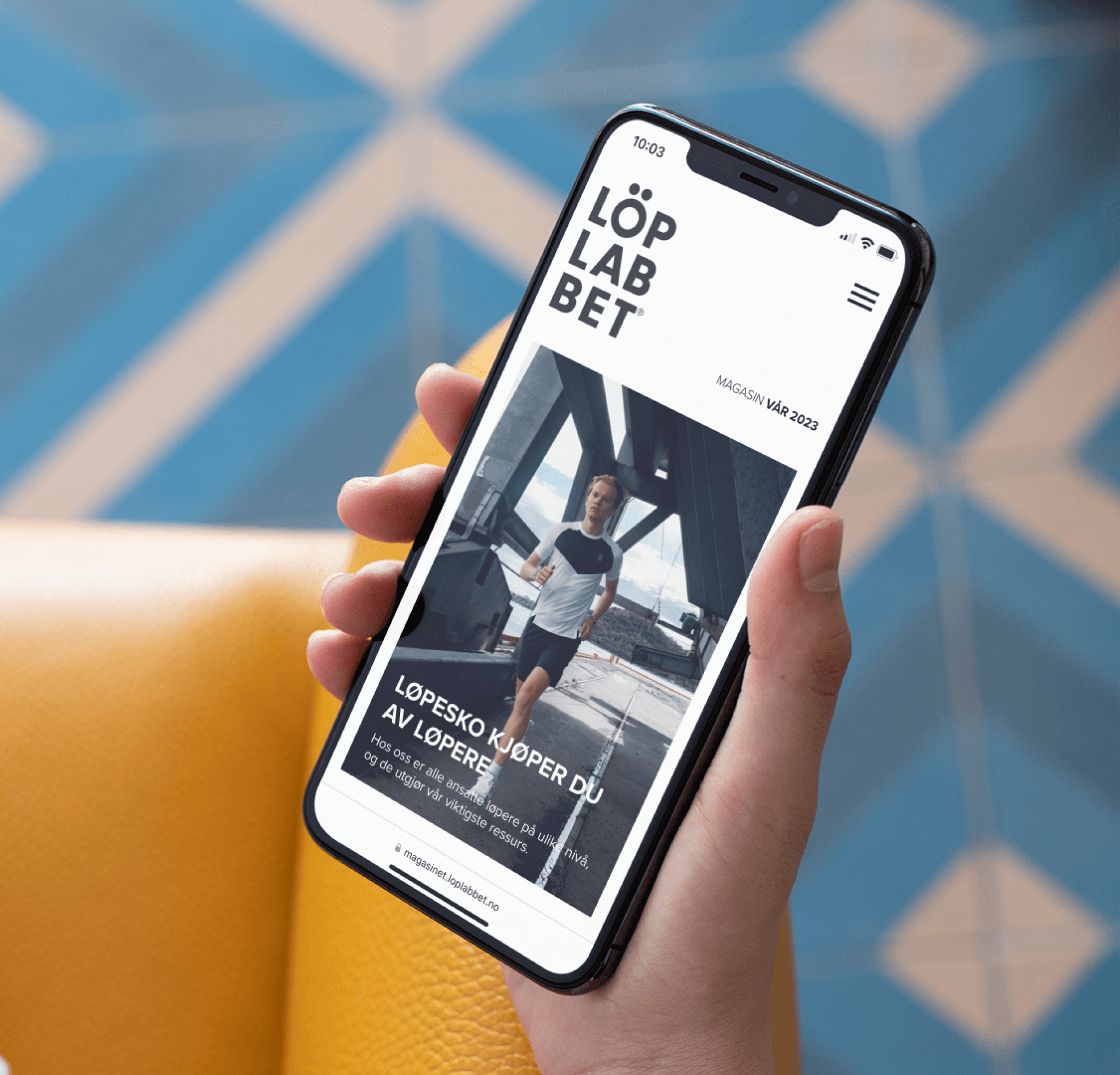 Phone mockup in a hand showing the frontpage of Löplabbets digital magazine spring edition 2023.