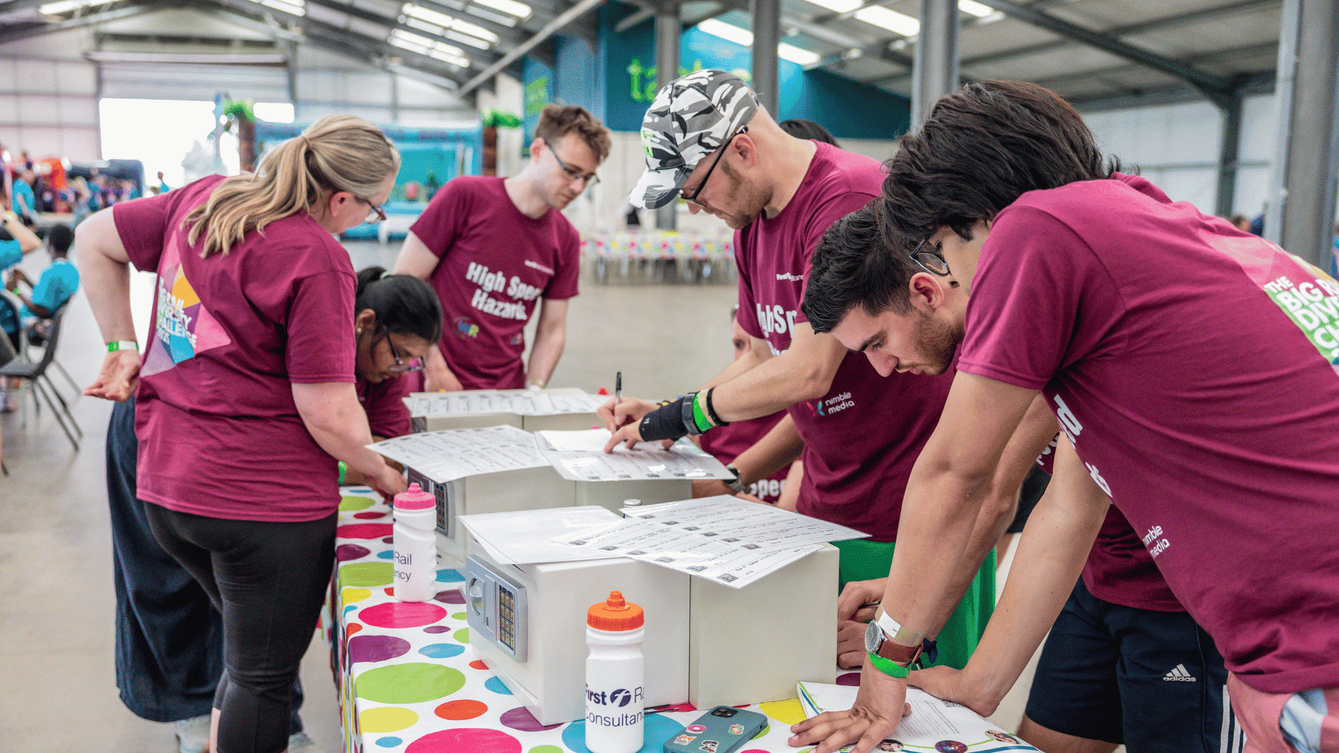 Outdoor team-building event with participants wearing matching blue shirts, taking part in inflatable obstacle courses and games, smiling and cheering, with the words 'ENTER A TEAM' in large bold white and green text across the image.