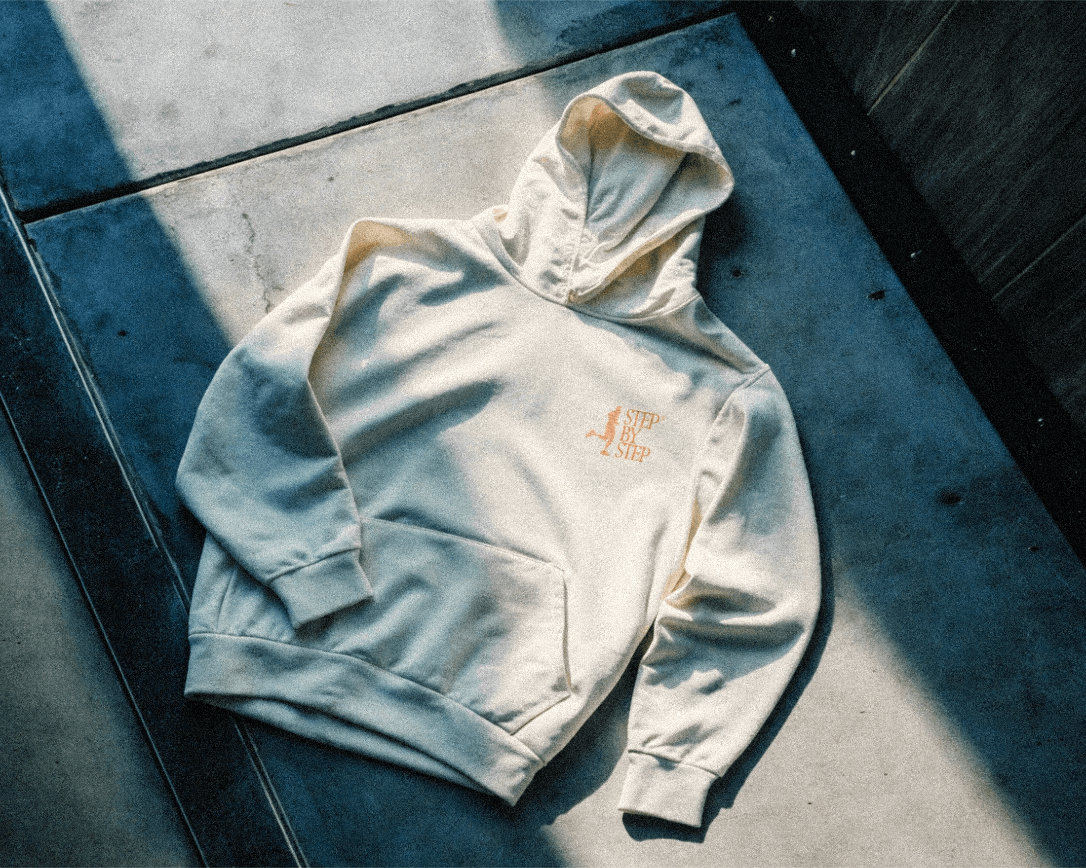 A hoodie laying flat on  a concrete pavement. The hoodie has the Step-by-step Running Club logo printed on it.