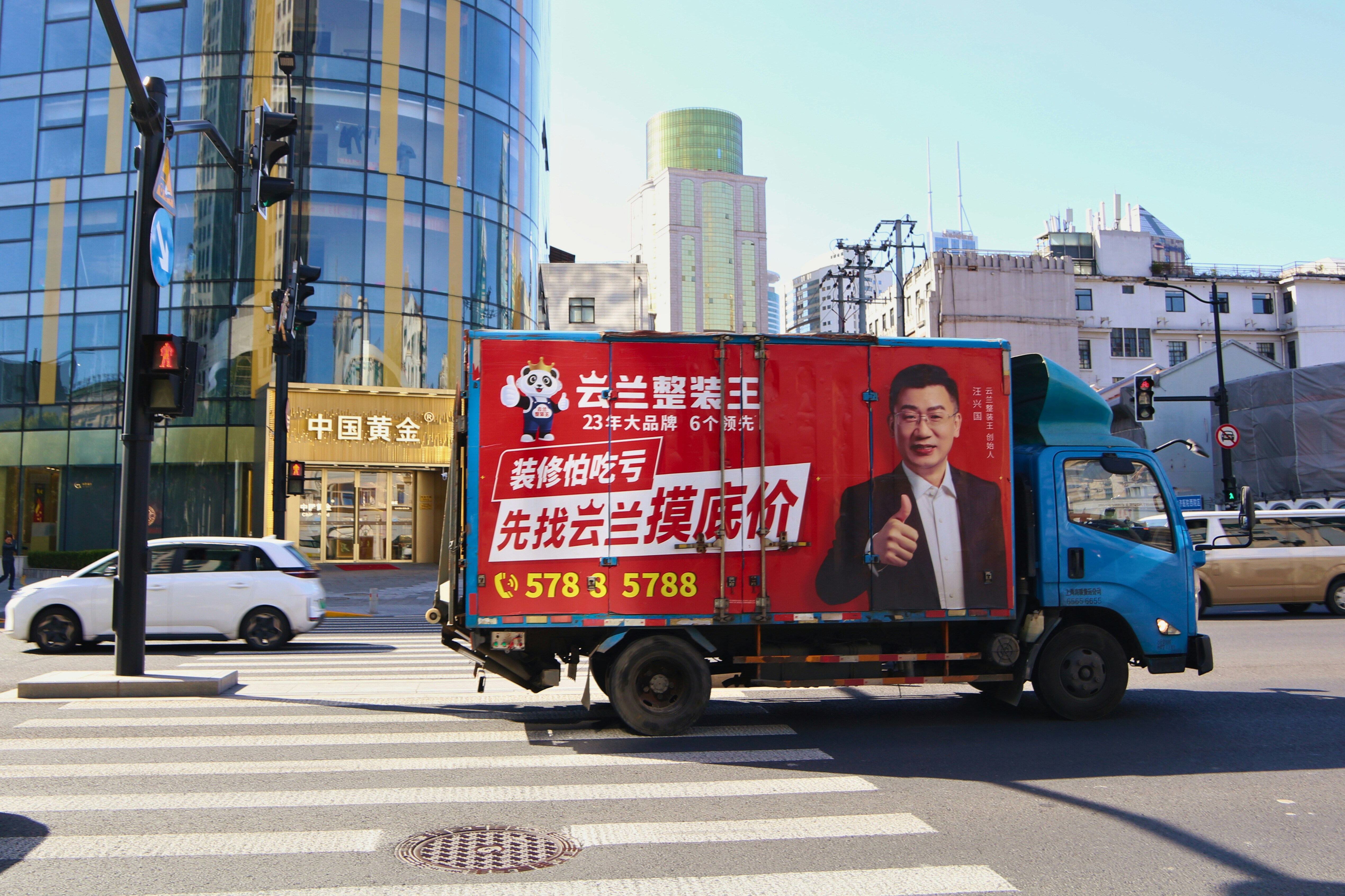 Blue truck with red advertisement drives on street.