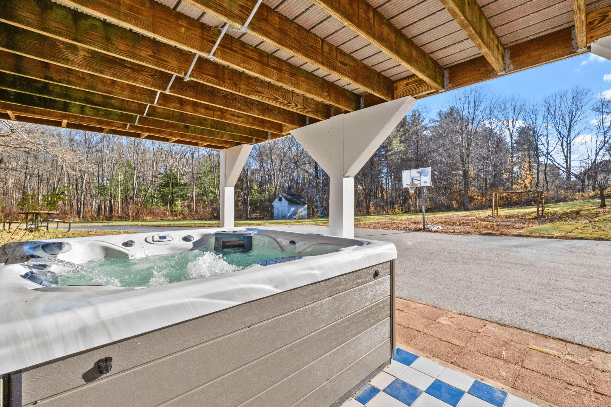 Outdoor hot tub on a covered deck overlooking a wooded private lot, offering a relaxing retreat for families or groups at this Lodgism-managed Airbnb home in Northborough, MA.