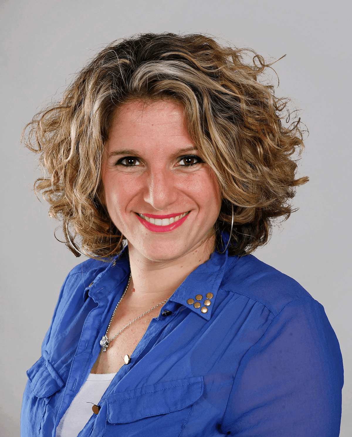 Minimal studio portrait of a confident woman in a white shirt, arms crossed, on a soft gray background.