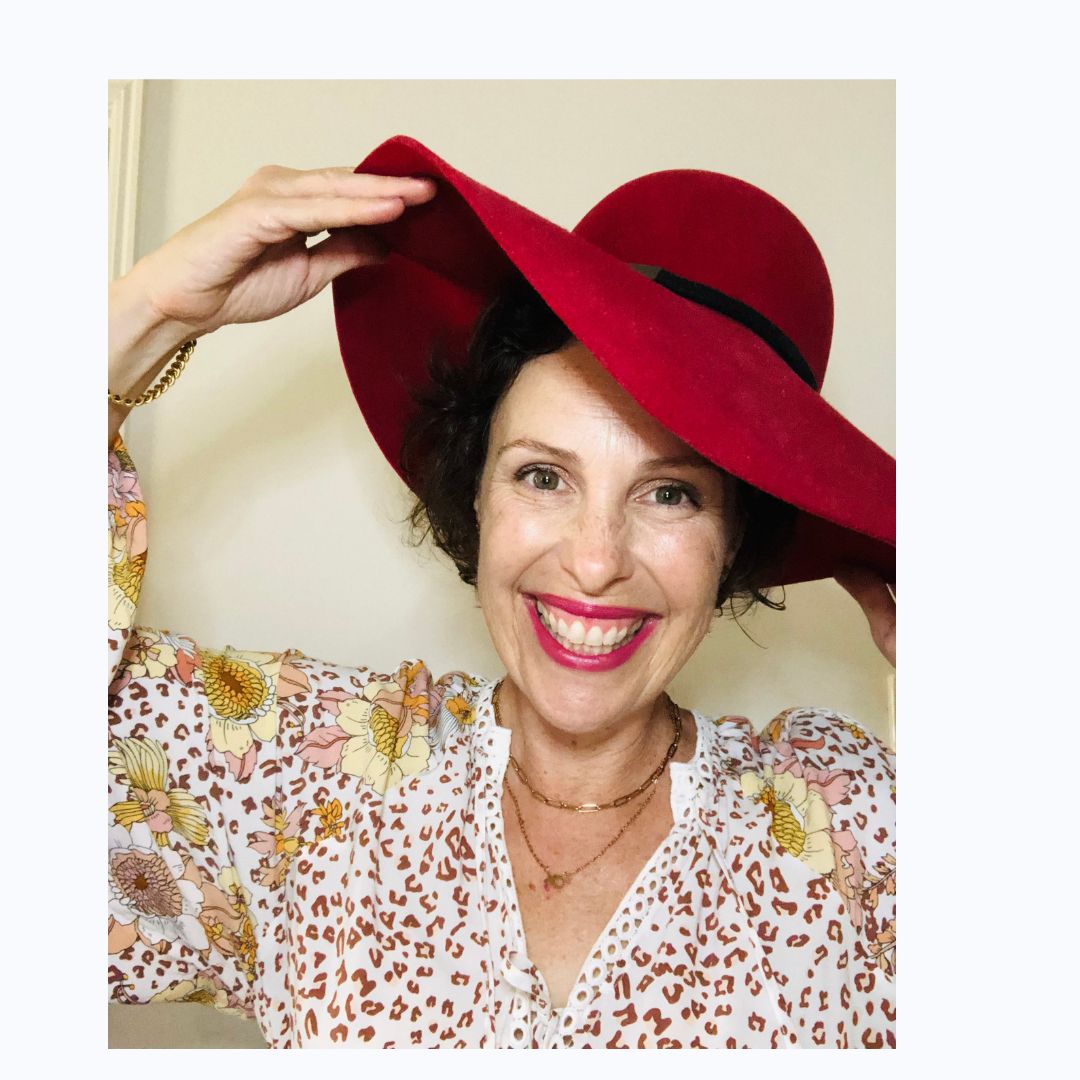 Smiling female therapist with short gray hair, wearing a brown top and a purple shawl, surrounded by a cozy background.
