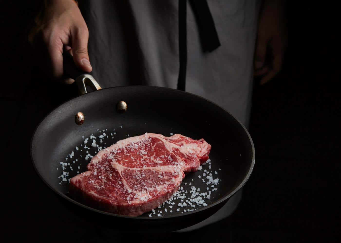 Person cooking a raw steak on a pan with salt