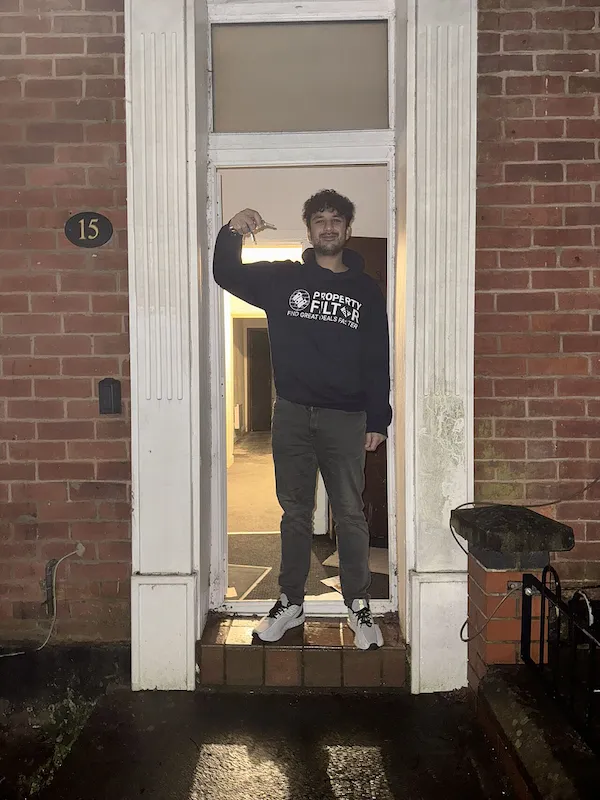 Person standing in the doorway of a brick house holding what appears to be keys