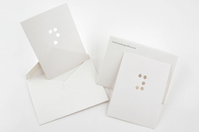 Two white cards are shown on a white background. The left card is partially folded and displays three small holes near the top. The right card is unfolded and shows four small holes near the top. The website address "www.touchingyellow.com" is printed on the top right corner of the right card.