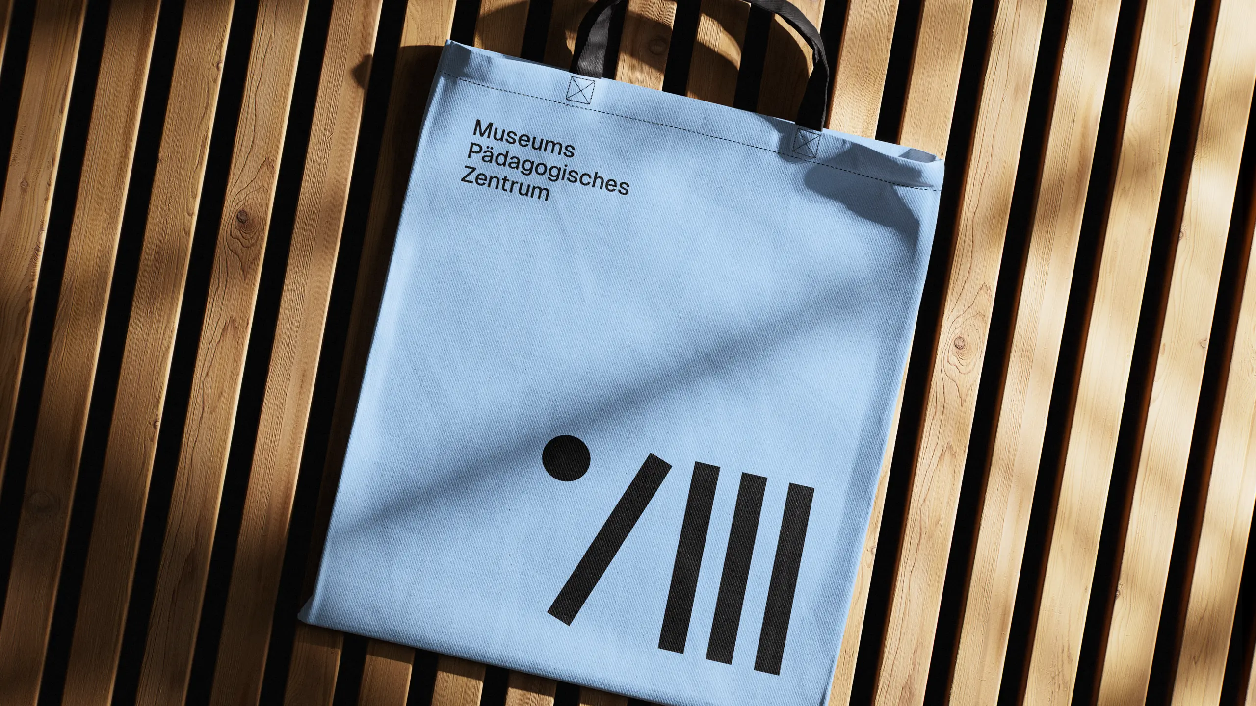 Hellblaue Stofftasche mit MPZ-Logo auf Holzbank in Sonnenlicht