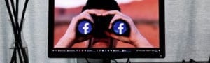 A man holding up binoculars with the Facebook logo on it