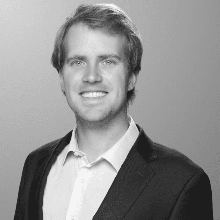 Black and white photo of the upper part of a white male in a suit with a light-colored shirt, smiling to the camera. This is the Director of Business Development, Matias Oberpaur