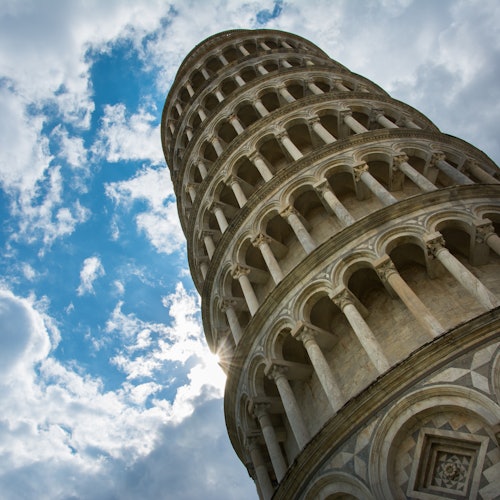 Leaning Tower of Pisa against a backdrop of blue sky with scattered clouds. Sunlight peeks through the arches.