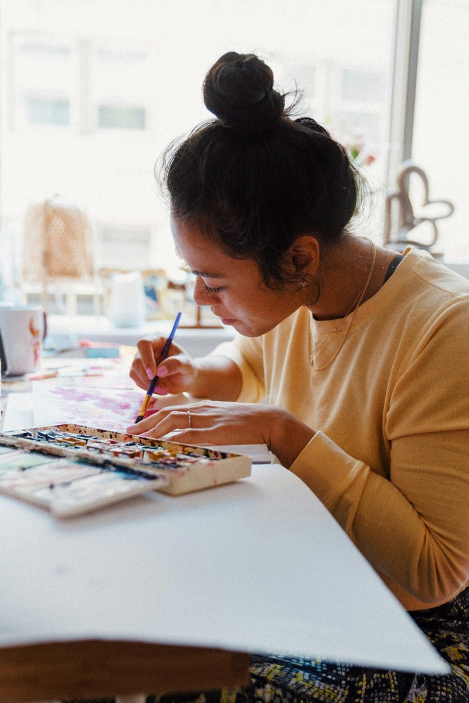 A woman working on a craft project with paints at a desk in a light room