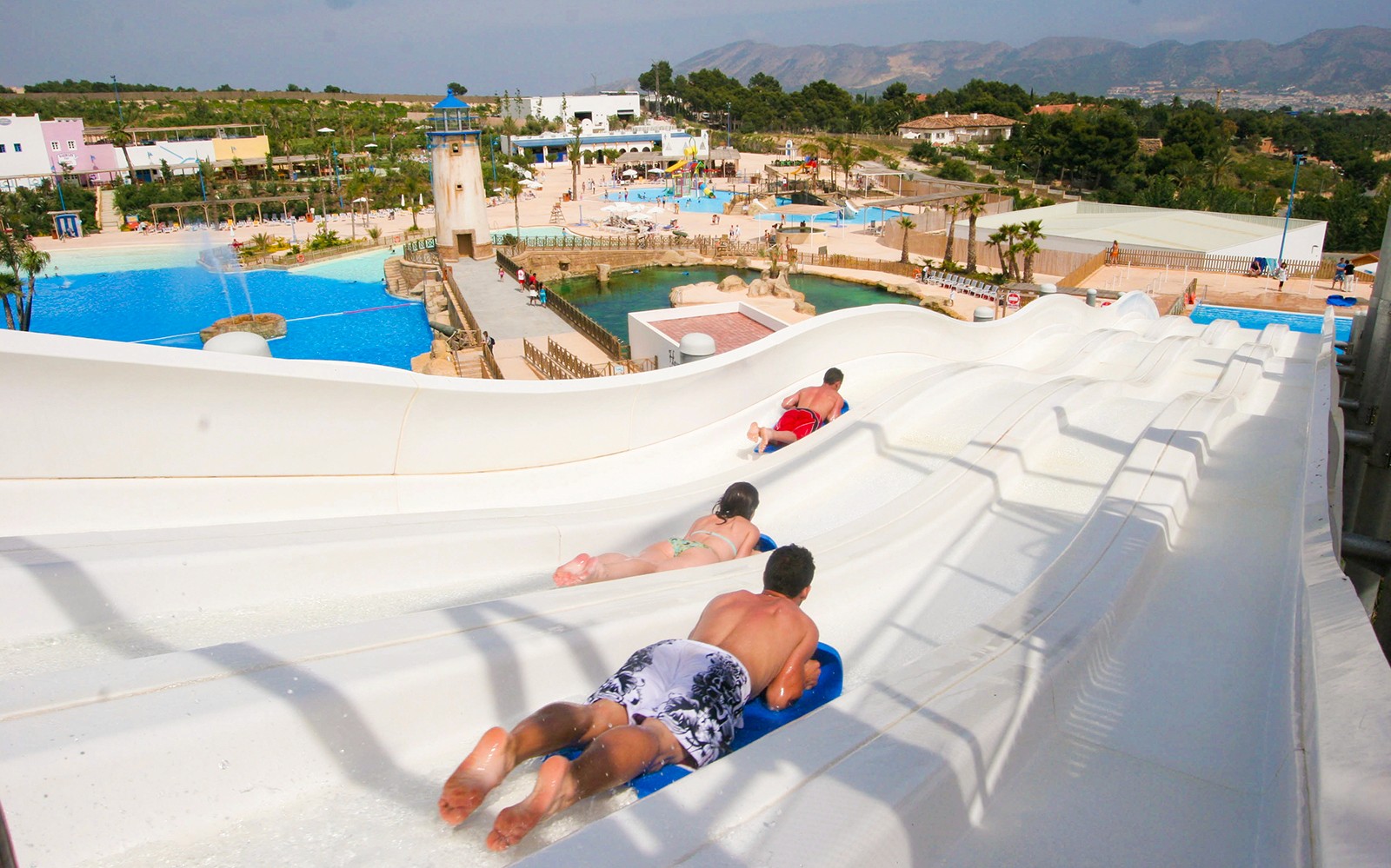 Visitors sliding down water slides at Terra Natura Benidorm with pools and landscape in view.