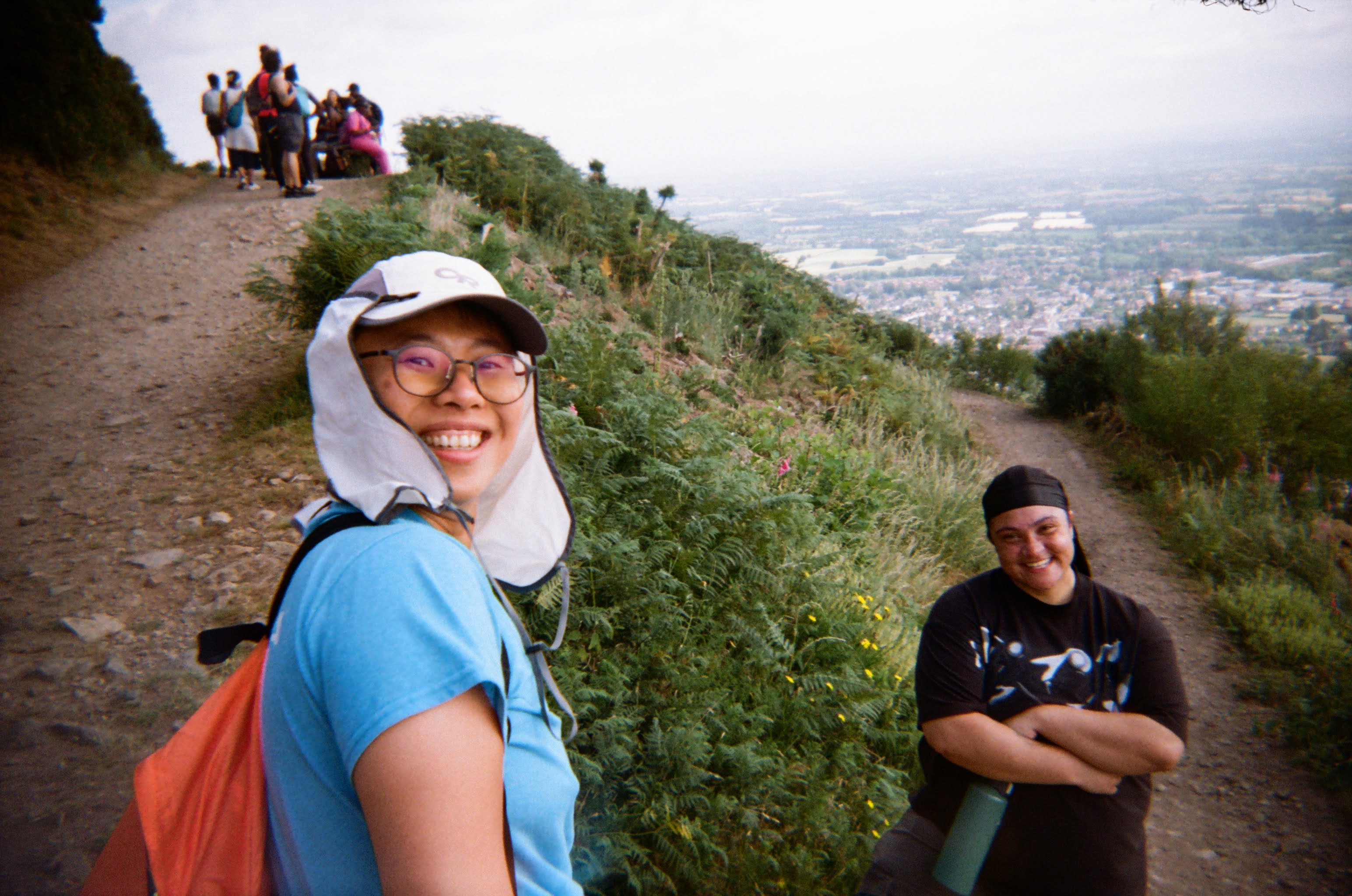Two people smile at the camera whilst at the top of a hill, after a hike