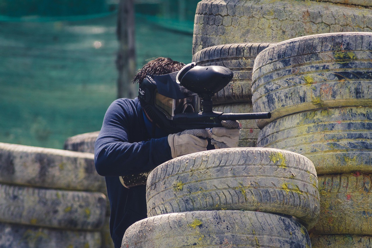 man playing paintball behind tyres