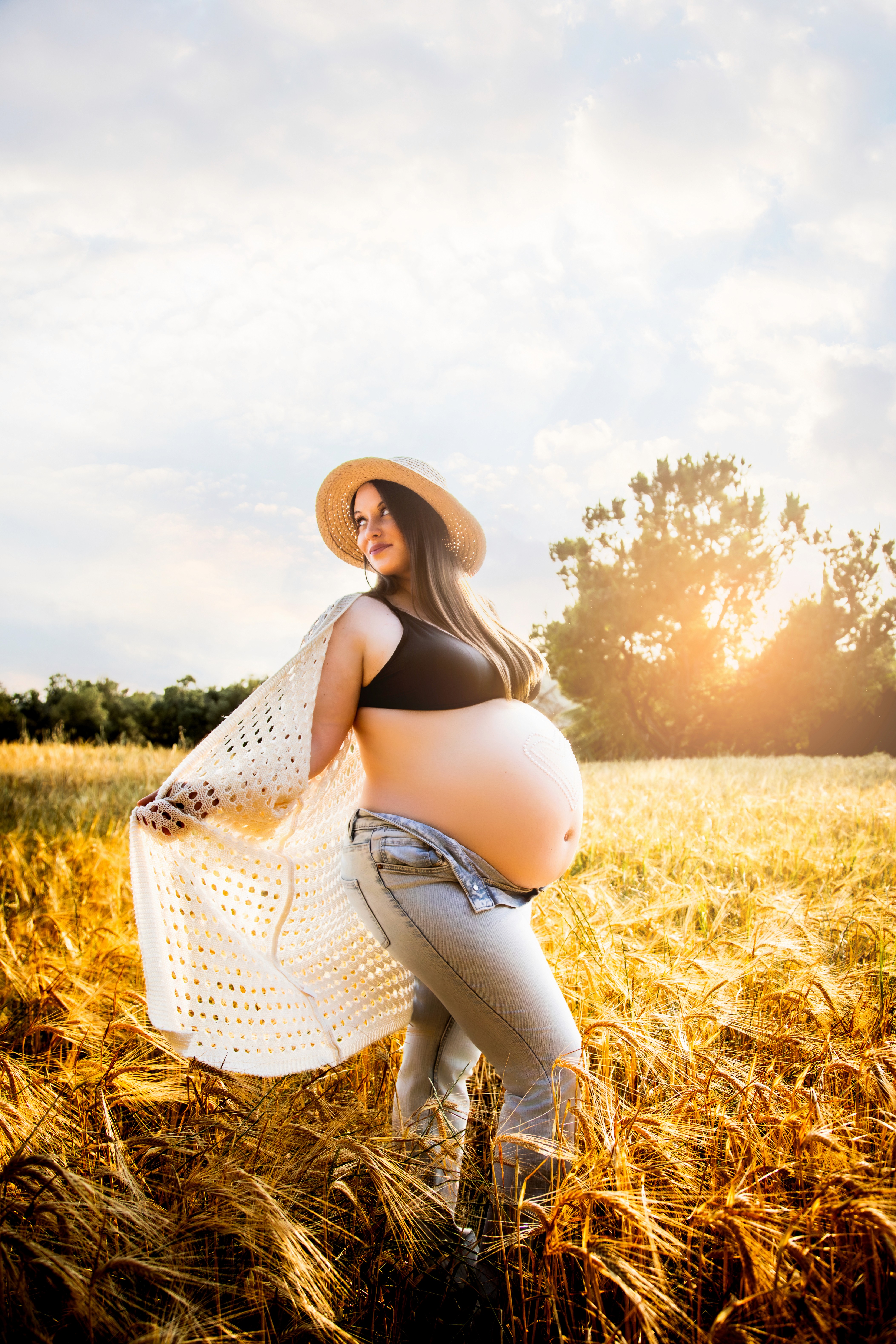 Premamá en un campo de trigo moviendo la camisa