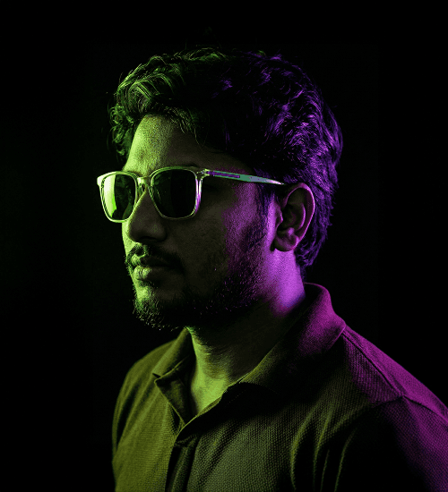 Lead Producer Prashanth B, wearing sunglasses and a collared shirt in low-key neon lighting.