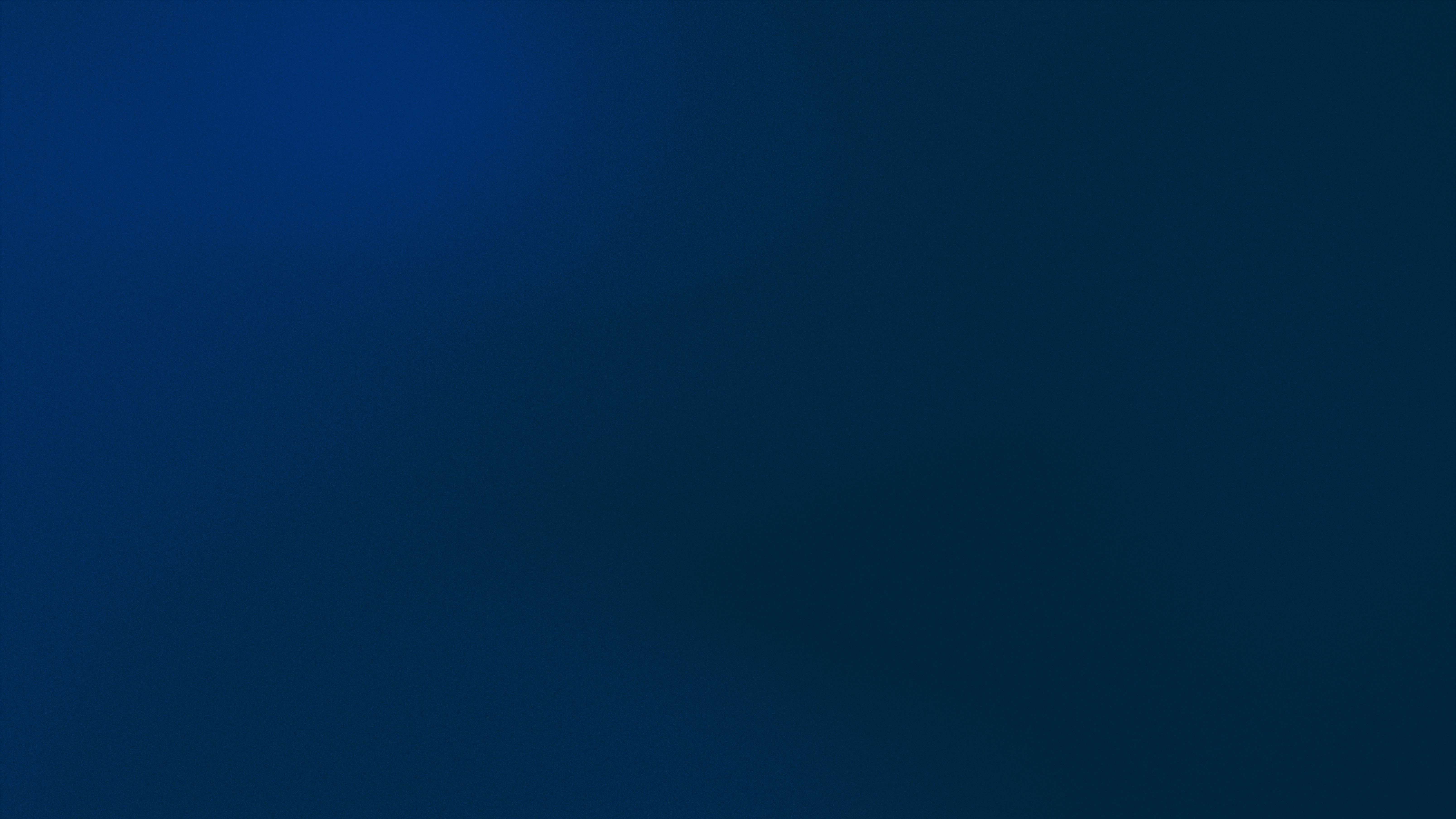 A man stands while two people sit at a table in an office setting, smiling and engaged in conversation. The mood is friendly and collaborative.