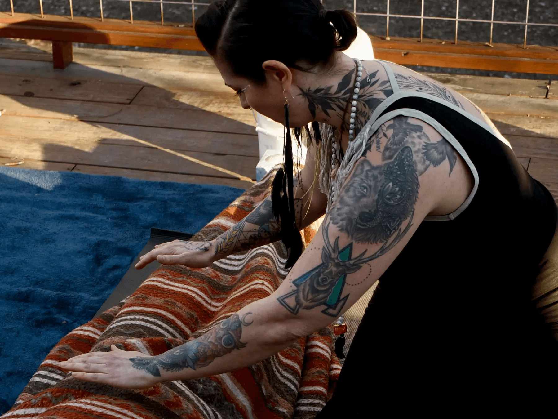 A person with tattoos is gently working on a colorful fabric on a wooden surface outdoors.
