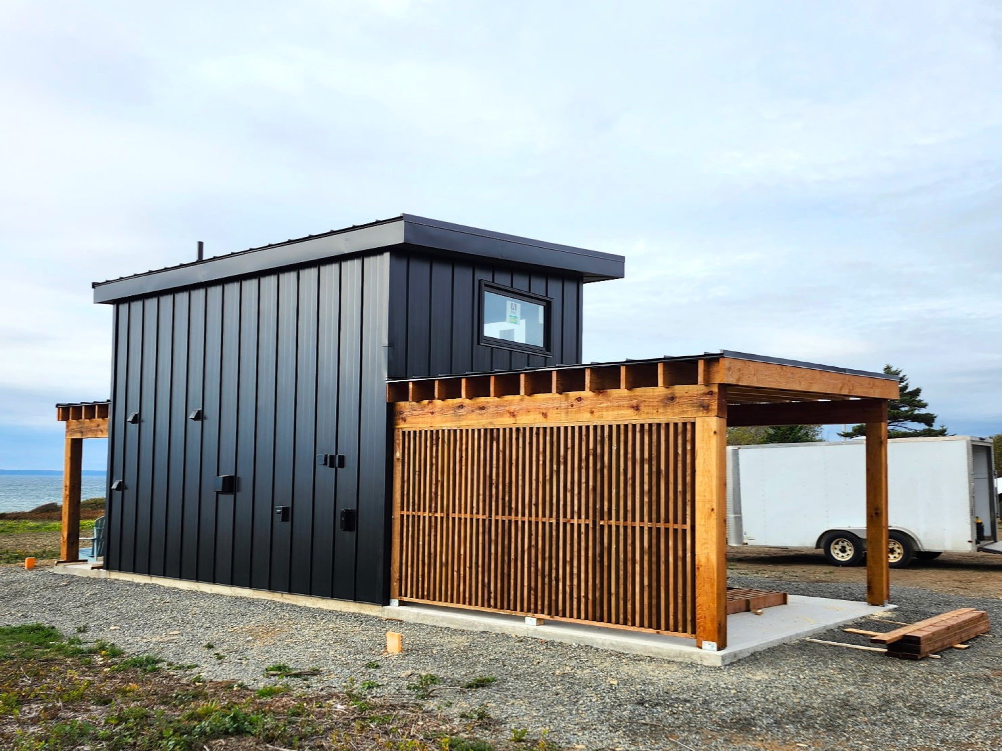 Completed tiny home at the Bogden property, dark clad with a cedar screen and covered deck