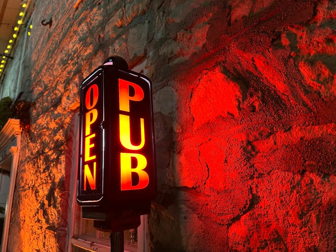 a pub sign lit up against a stone wall