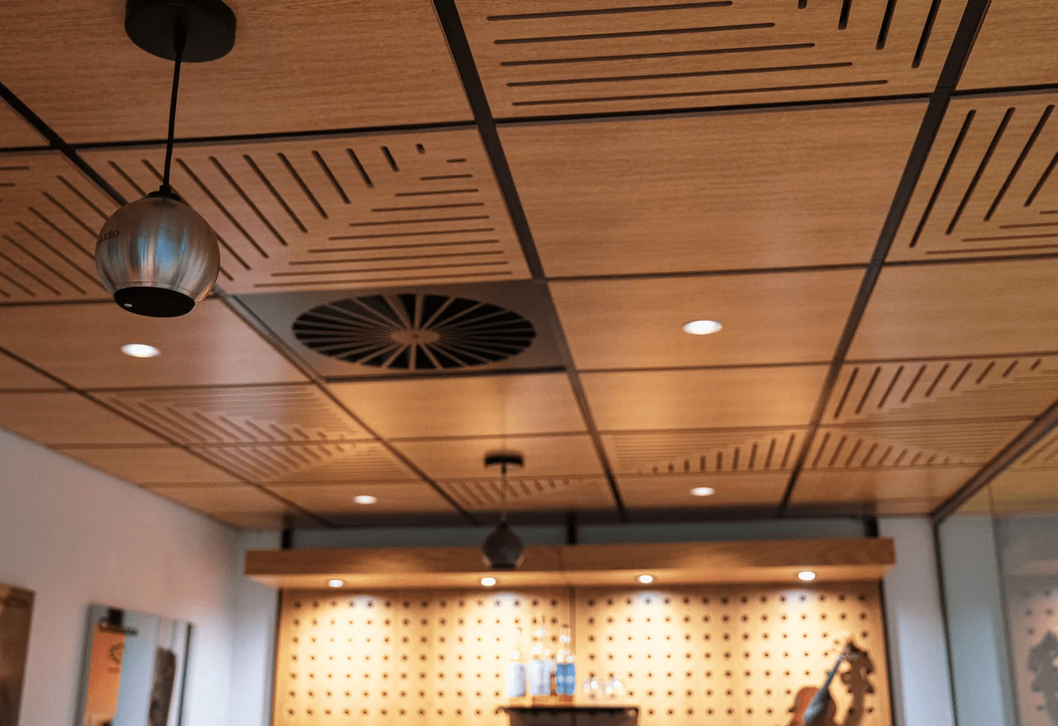 Wood panel ceiling with geometric designs, vents, and lights