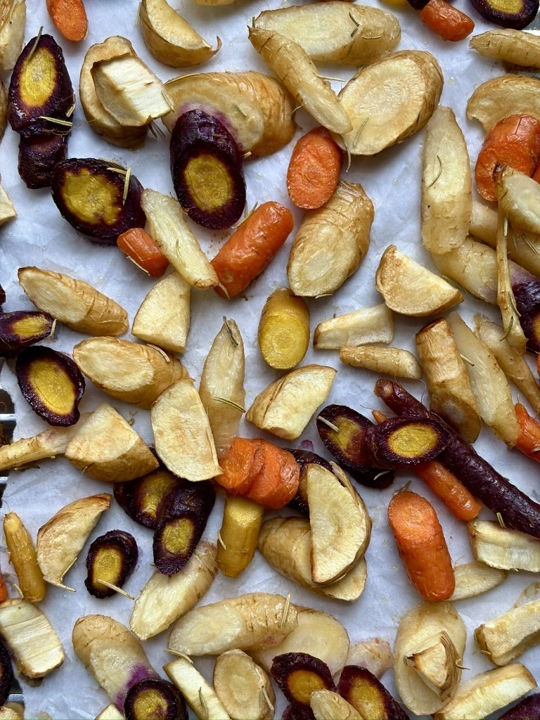Roasted rosemary root vegetables on a sheet pan, including golden, caramelized sliced carrots and turnips, lightly coated in olive oil and rosemary, finished with a squeeze of fresh lemon.