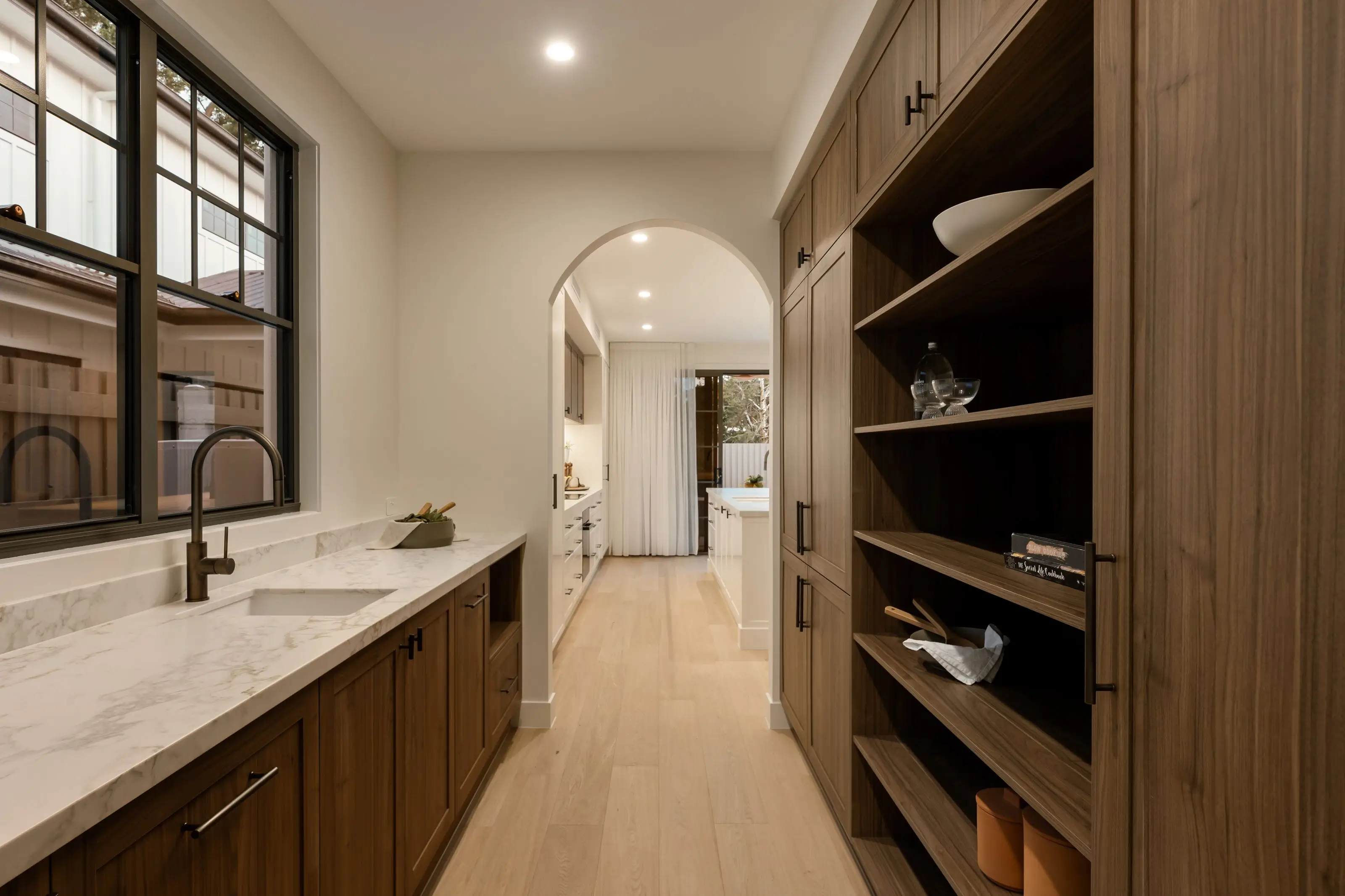 Luxury butlers pantry with kitchen visible through arched doorway