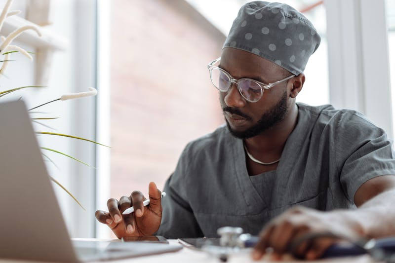 a dentist wearing glasses uses his phone and laptop