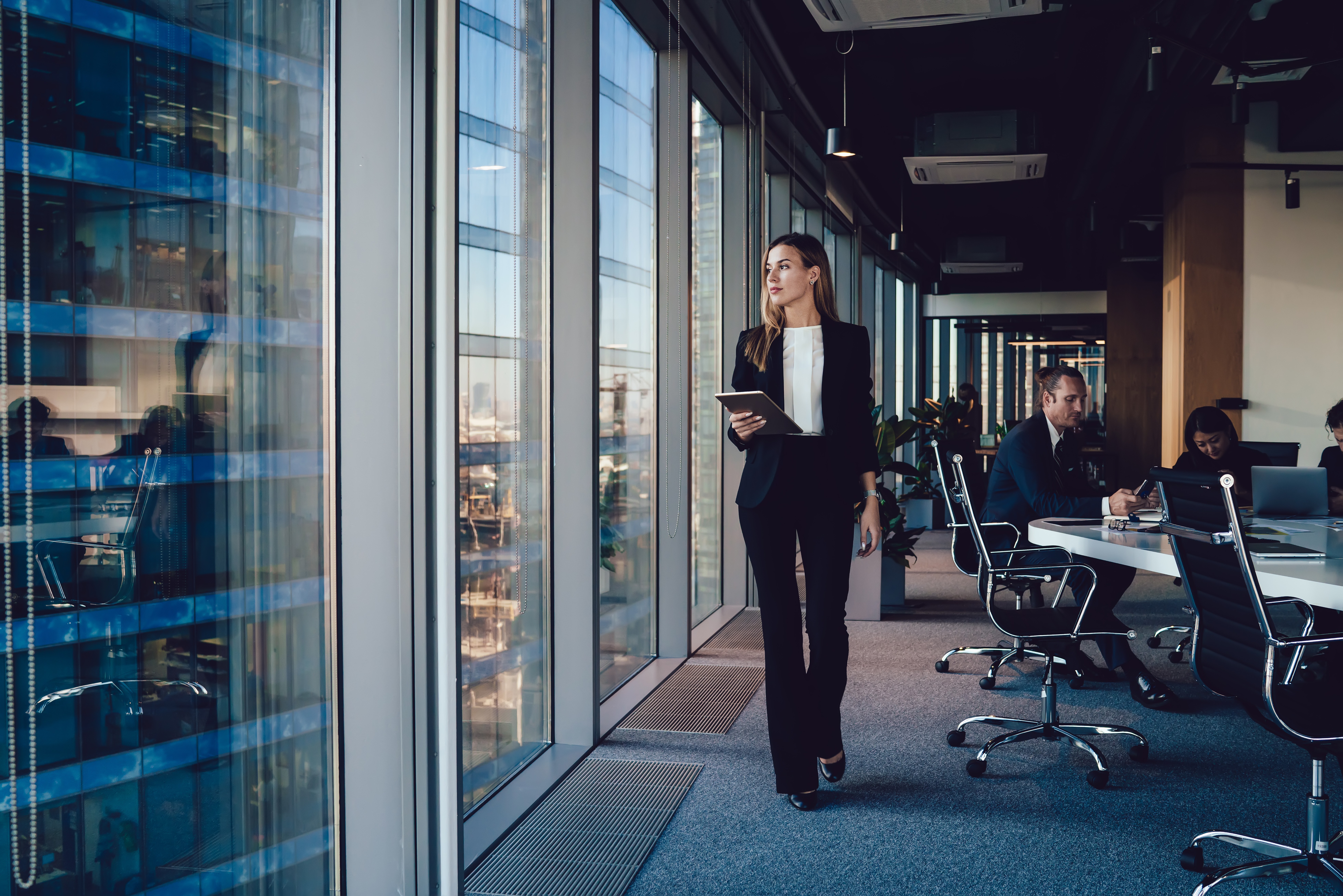 Serious female administrative manager in formal suit walking in office with digital tablet