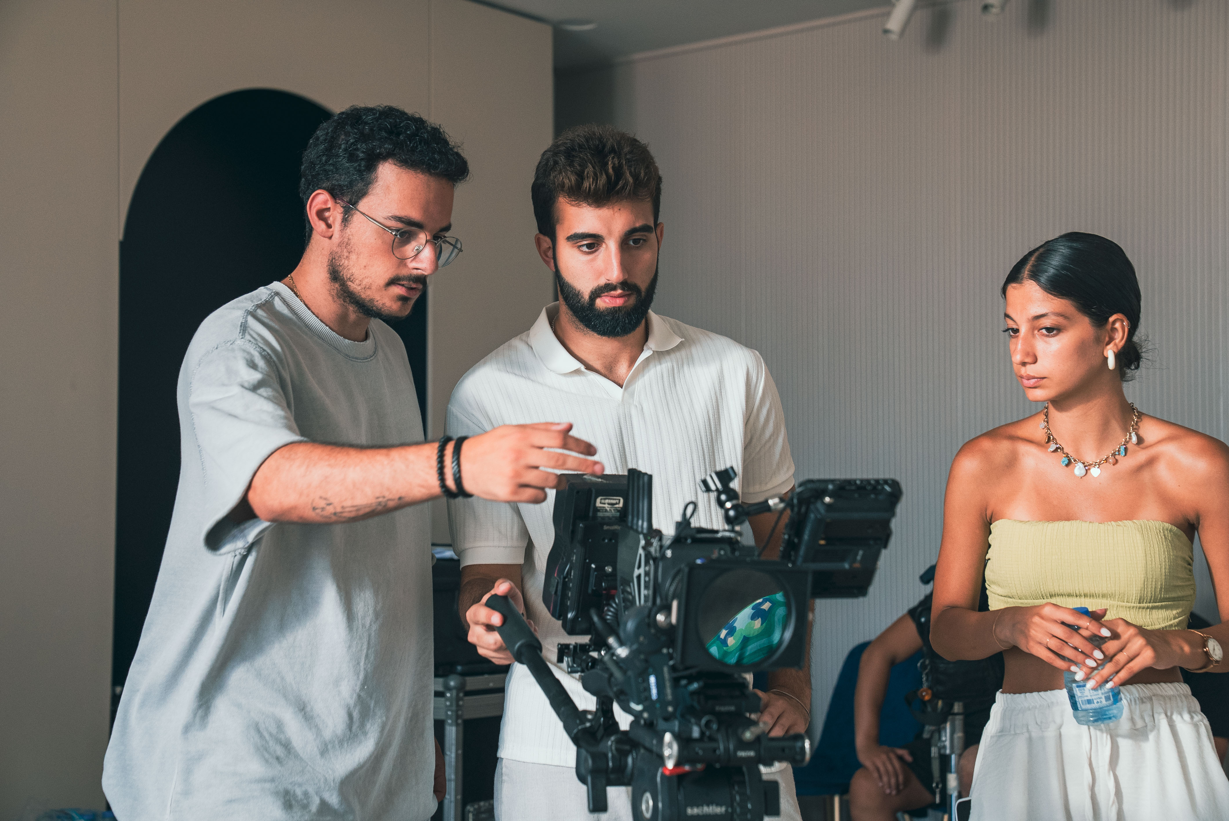 Three people in conversation with warm lighting, including a person wearing a hat and another person wrapped in what appears to be a textured shawl or sweater.