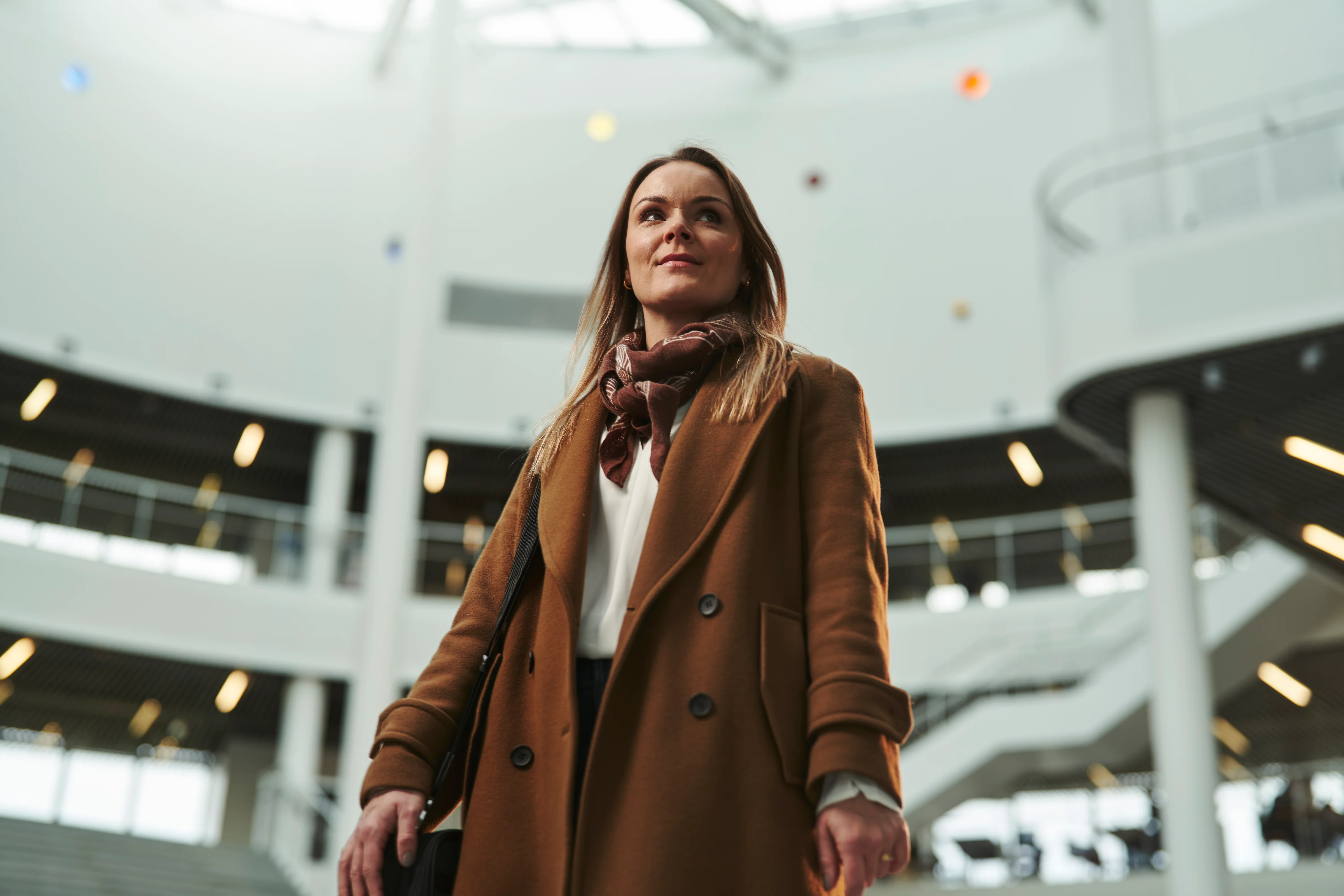 A professional woman inside Reykjavík University, standing in a bright, modern atrium with open staircases and natural light.