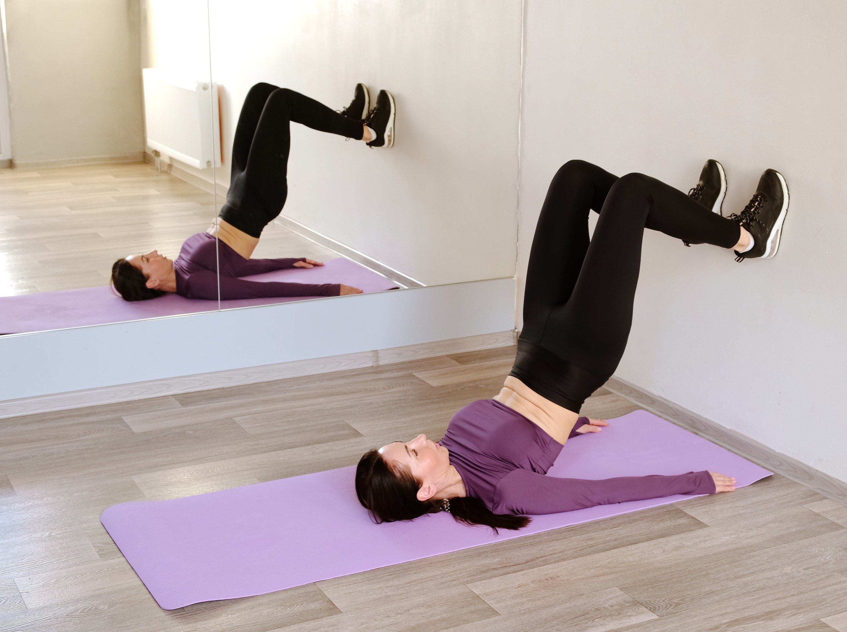 woman doing wall pilates for weight loss by herself with a yoga mat in a bright studio