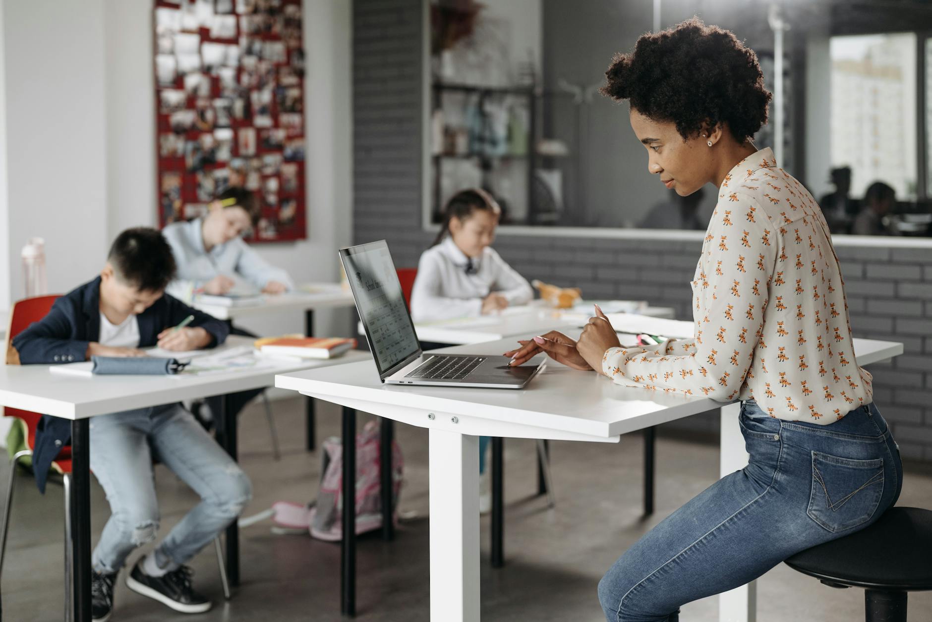 A close-up of a teacher's hands holding a steaming mug of coffee next to an open planner and a heart-shaped paperweight.