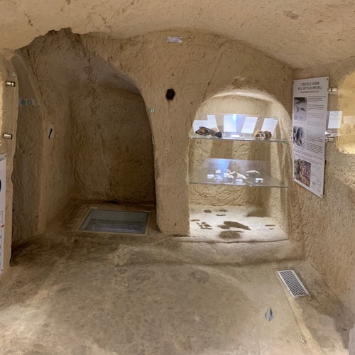 Underground cave exhibit with skulls and bones displayed on glass shelves, information panels on walls, and a small opening.