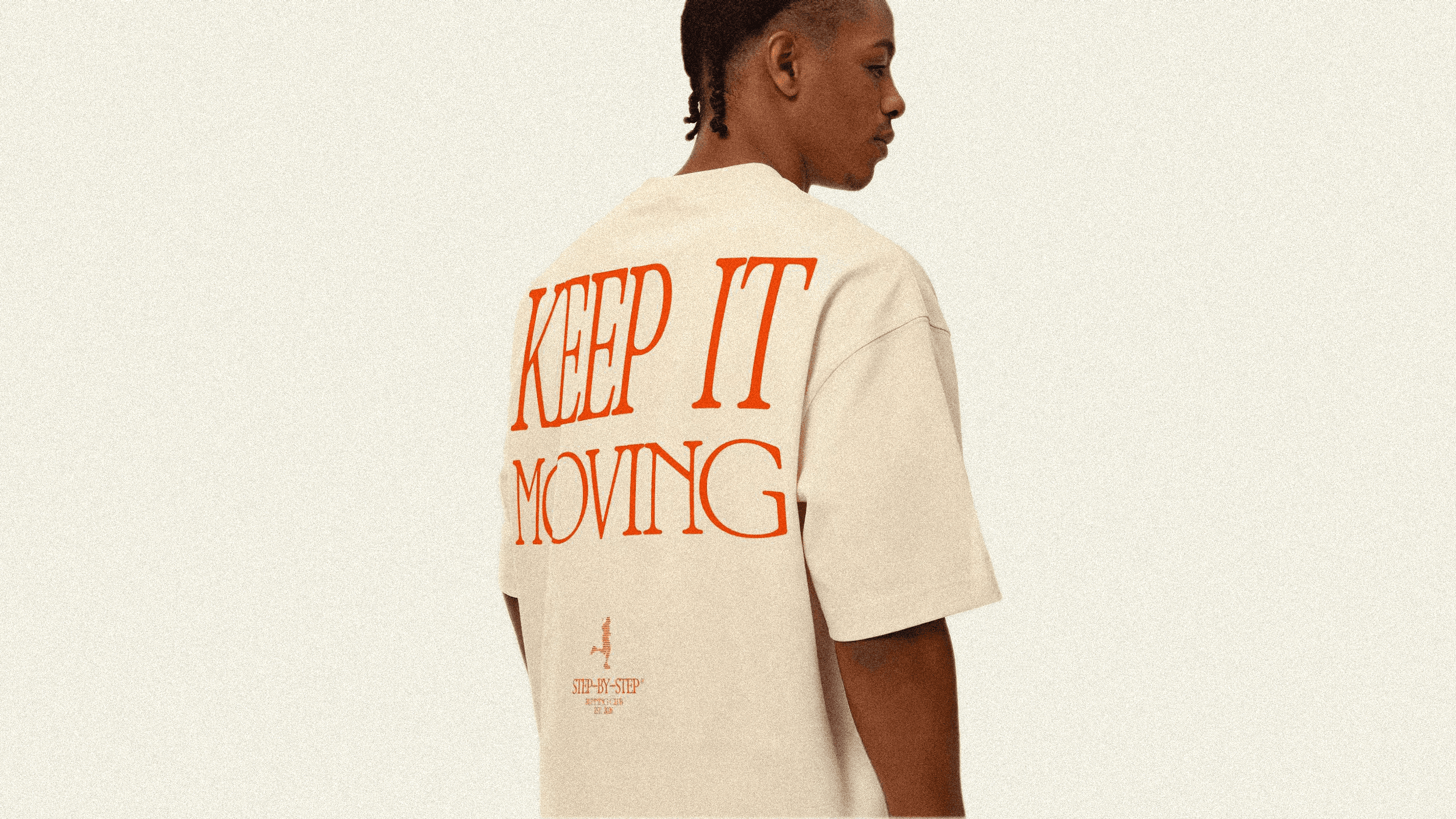 A man wearing a cream-colored t-shirt with the words "KEEP IT MOVING" printed on the back in bright orange.
