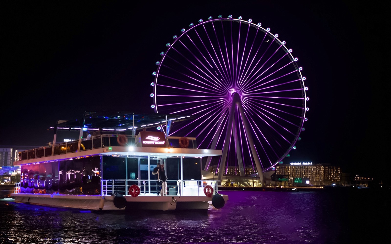 Hausboot auf dem Wasser mit dem Ain Dubai Riesenrad, das nachts beleuchtet wird.