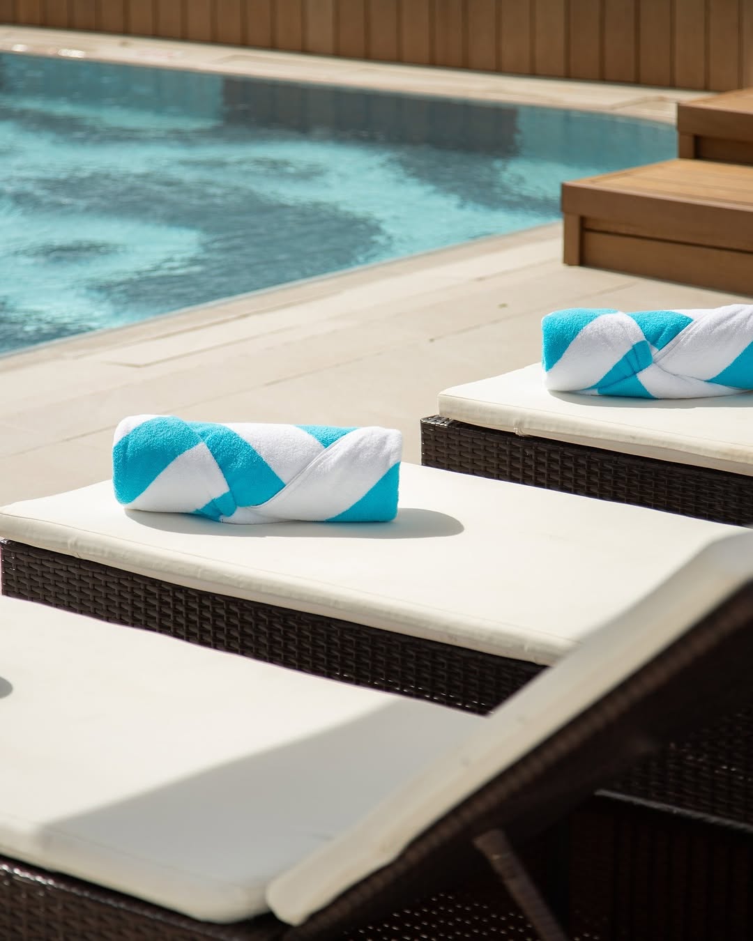 Poolside scene featuring neatly rolled turquoise and white towels on lounge chairs, beside a clear swimming pool.