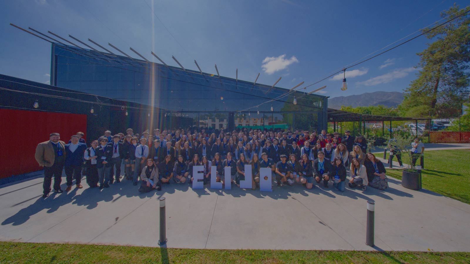 Estudiantes escolares posan en grupo alrededor de letras grandes que forman la palabra ELIJO en un evento de IdeaPaís.